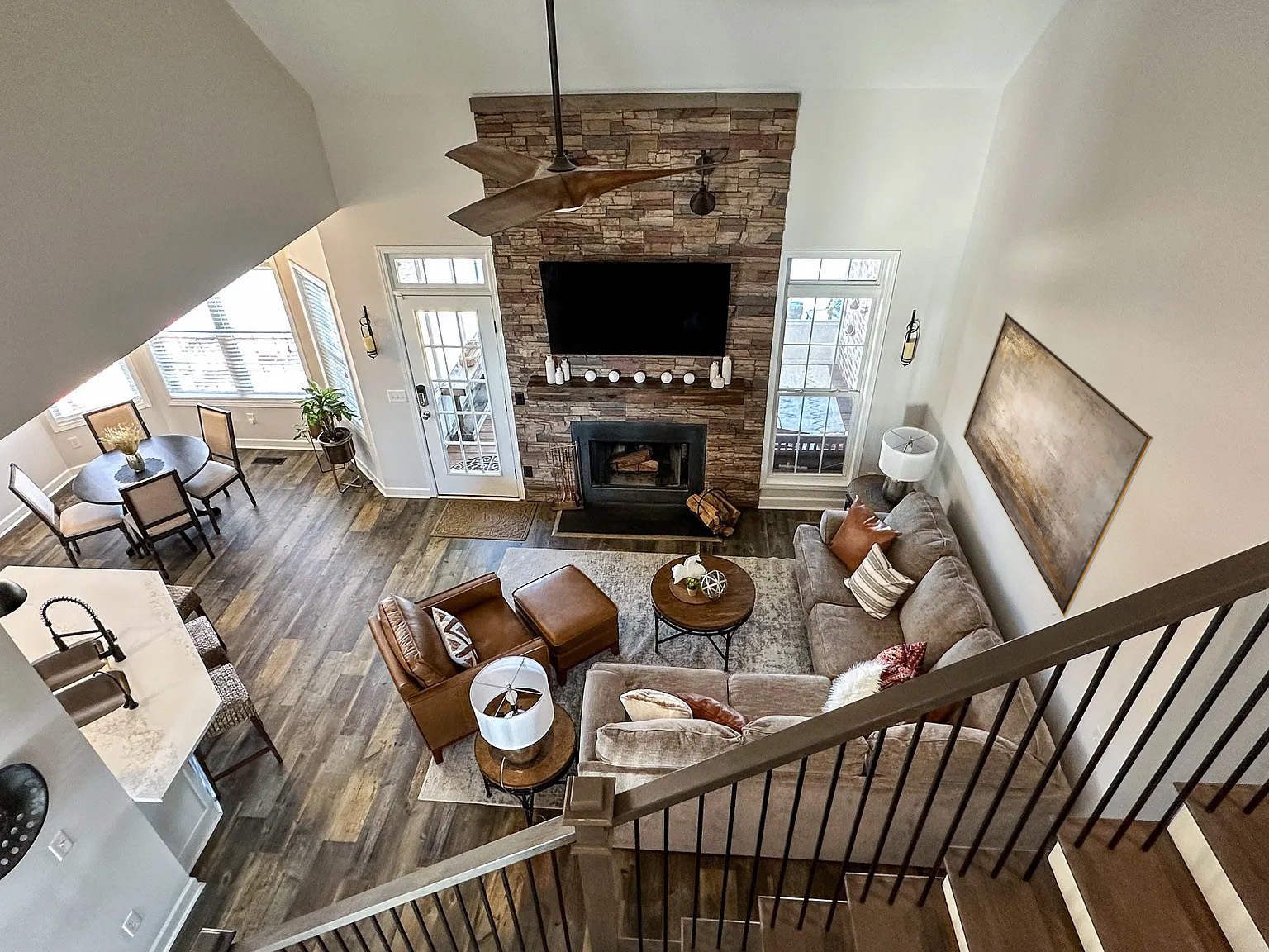 Two-story great room with stone fireplace, staged with warm leather and neutral furnishings